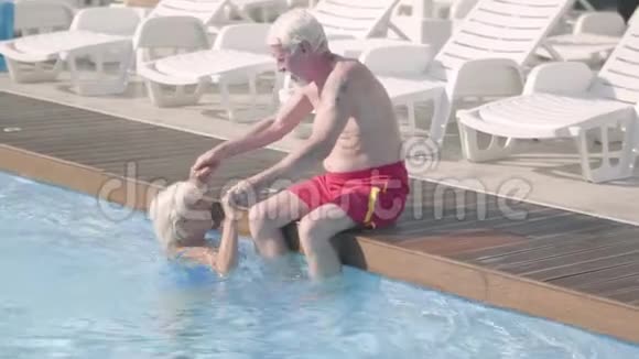 快乐的成熟夫妇一起在酒店综合体的游泳池放松坐在游泳池边上的老人视频的预览图