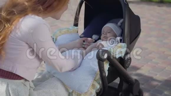 年轻快乐的红头发母亲和婴儿在马车里说话在美好的春天里微笑着照顾他视频的预览图