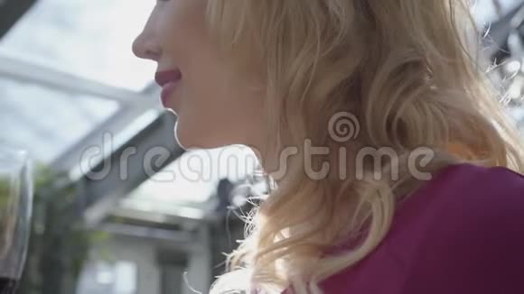 年轻漂亮的金发女人在阳光的映衬下从酒杯里喝红酒关门视频的预览图
