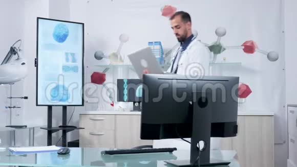 他现代办公室里的医生站在他的笔记本电脑上打字视频的预览图