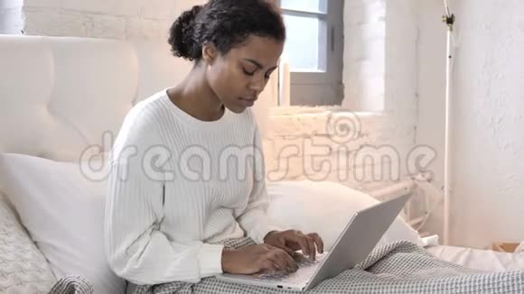 背疼的非洲青年妇女在床上做手提电脑视频的预览图