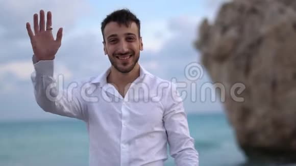 一个成功的微笑男人的肖像穿着白色衬衫挥动着一只手英俊的胡子男站在海边视频的预览图