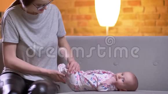 母亲给她可爱的新生女儿换尿布的肖像躺在客厅的沙发上视频的预览图
