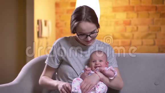 母亲抱着她可爱的新生女儿坐在客厅的沙发上的肖像视频的预览图
