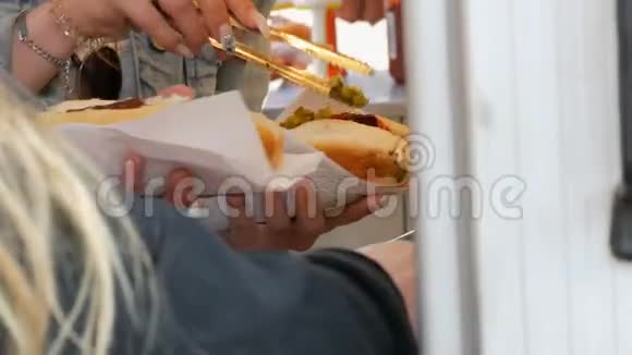 女孩们手把各种调料放在一只热狗上在阿姆斯特丹街上的街头食品快餐亭里视频的预览图