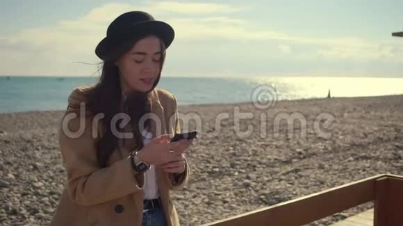 独自一个漂亮的女士在海边的智能手机上用无线上网聊天视频的预览图