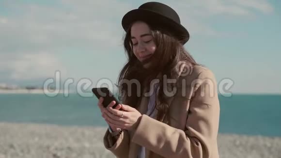 微笑的女人通过智能手机在网上聊天在海边上网视频的预览图