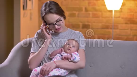 妈妈在智能手机上聊天和她可爱的女儿在客厅拥抱的特写肖像视频的预览图