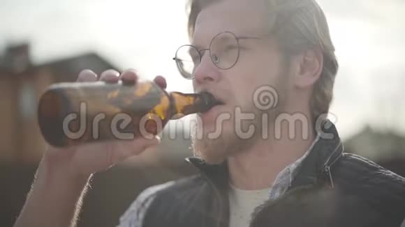 戴眼镜的大胡子男人在户外喝啤酒享受饮料他尝起来有啤酒味慢动作视频的预览图