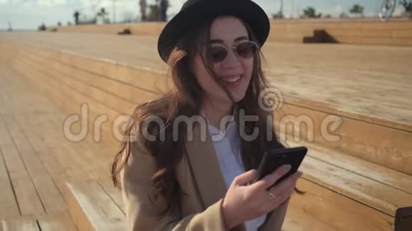 浪漫的快乐女孩正在智能手机上阅读短信在阳光明媚的日子里坐在户外视频的预览图