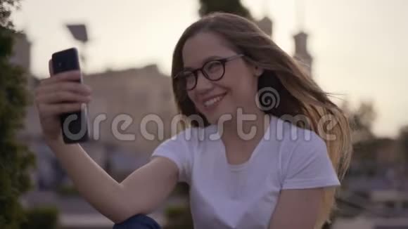 微笑长发女孩在视频聊天中与朋友使用手机公园里的女孩视频的预览图