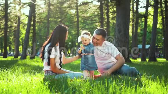 美丽的蹒跚学步的女孩和父母一起享受阳光公园绿草的夏天视频的预览图