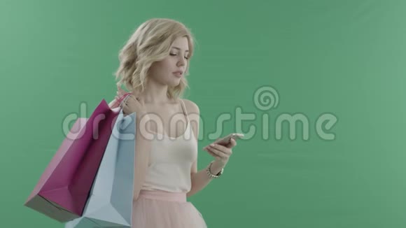 年轻有魅力的女人在等待一个拿着袋子对着绿色屏幕的人时用手机上网视频的预览图