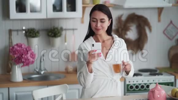 穿着白色浴袍的女人在手机上发信息用手机在家工作视频的预览图