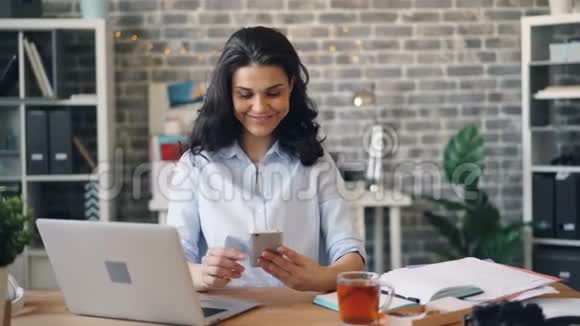 有智能手机的女人在工作中享受社交媒体触摸屏幕微笑视频的预览图