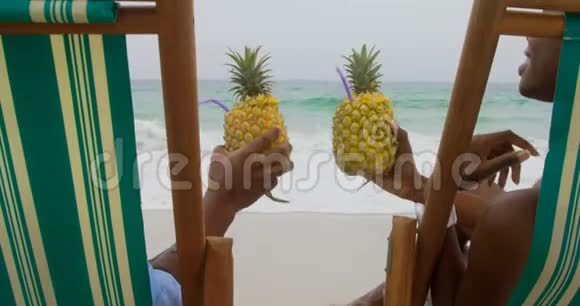非裔美国人夫妇在海滩上品尝菠萝汁的后景视频的预览图