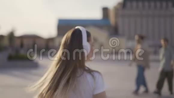 空中亲吻有趣的女孩在城里散步一大早大耳机吹吻的女人视频的预览图