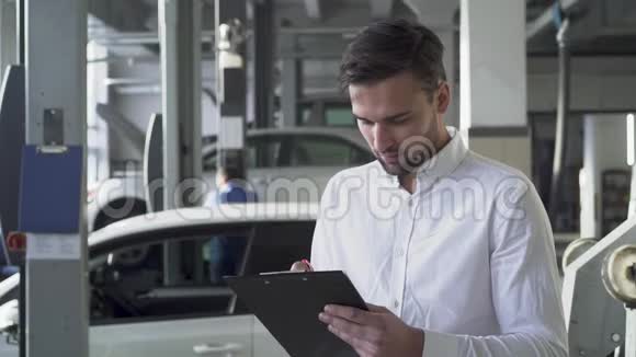 汽车服务部门的年轻帅哥在他的汽车背景上签署了有关汽车的文件并微笑着视频的预览图