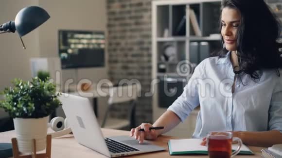 办公室里忙着看笔记本电脑的女孩坐在办公桌前看着屏幕视频的预览图