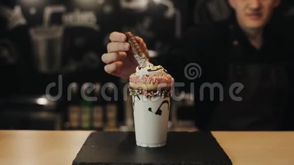 一个男咖啡师在一个疯狂的奶昔里放一个巧克力圆饼和一个甜甜圈和鲜奶油视频的预览图