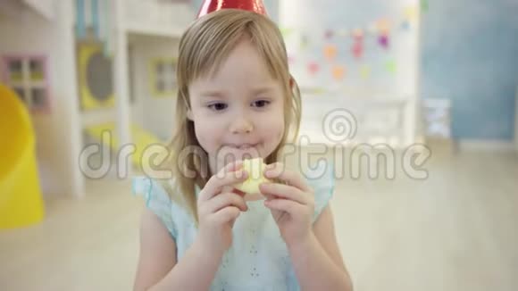 快乐的小女孩戴着节日锥帽在游戏室吃棉花糖视频的预览图