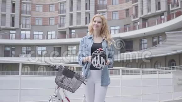 一位美丽的金发美女戴着自行车头盔在城市背景下骑着自行车视频的预览图