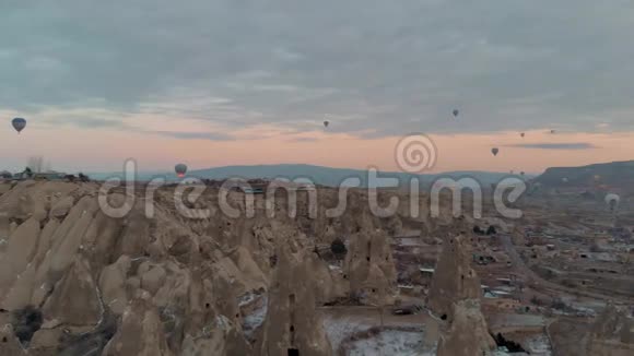 在卡帕多西亚日出时白雪皑皑的仙女烟囱上飘着五颜六色的热气球视频的预览图