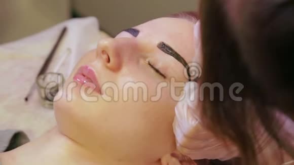 美容师用一种特殊的刷子画客户的眉毛并纠正它视频的预览图