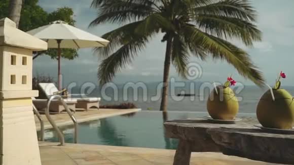 在无限游泳池和海洋前的木桌上放两杯椰子饮料视频的预览图