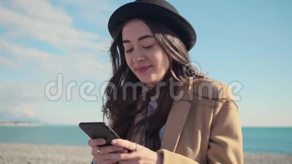 年轻的黑发美女的肖像是通过智能手机在海岸地区发送信息的视频的预览图