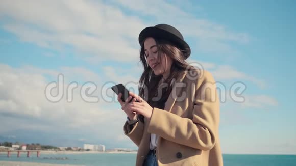 在阳光明媚的天气里布鲁内特女士正在海边地区用智能手机发短信视频的预览图