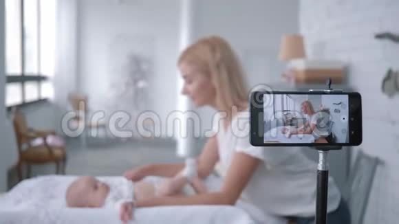 产妇护理妈妈vlogger在手机上录制培训视频的同时教孩子如何换衣服视频的预览图
