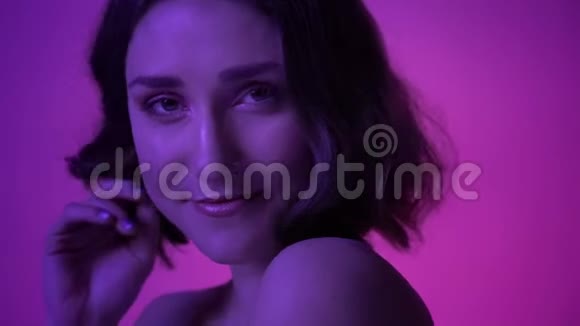 拍摄的特写镜头是年轻漂亮的女性在镜头前摆弄她的头发背景为霓虹灯紫色视频的预览图
