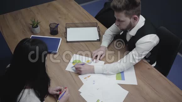 一个穿着正式服装的男人给坐在桌子旁的女同事穿着带有图表和模式的演示文稿视频的预览图