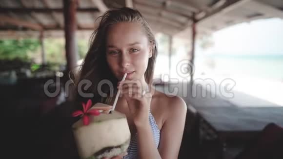 在海滩别墅下喝椰子的女人直视镜头视频的预览图