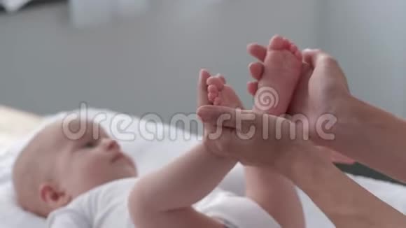 妈妈抱着女儿的小腿然后轻轻地抚摸和亲吻快乐的宝宝躺在餐桌上视频的预览图