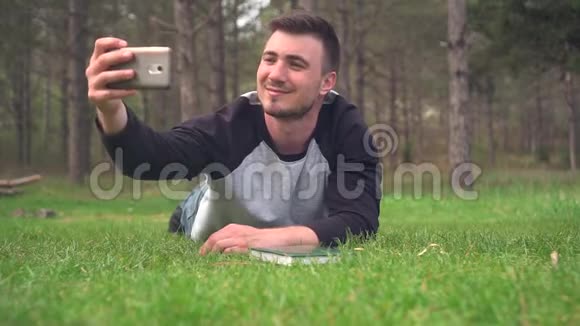 一个年轻人躺在森林里的绿草上在电话里自拍休息放松愉悦视频的预览图