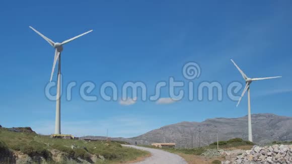 阳光明媚的一天两台风力涡轮机和道路在山丘景观之间视频的预览图
