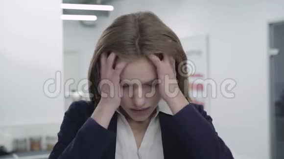 一幅穿着正式服装的悲伤疲惫的年轻女士站在办公室里抓着她的头发用一个视频的预览图