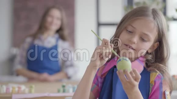 肖像美丽的小集中女孩长发蓝色围裙画复活节彩蛋小刷子在里面视频的预览图