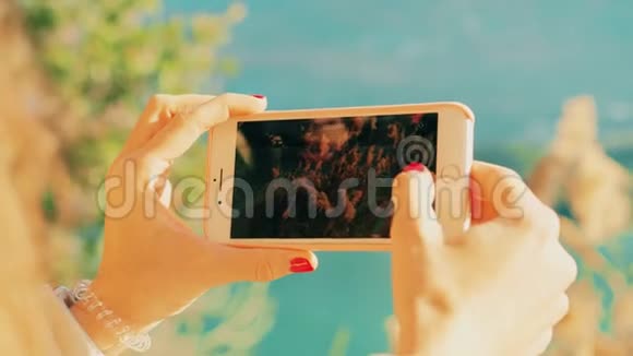 年轻女子用智能手机在湖岸拍摄风景视频红色摄像机拍摄视频的预览图