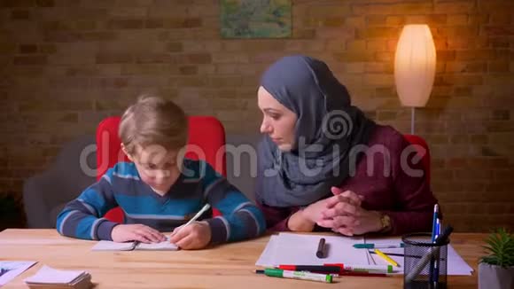 穆斯林母亲戴着头巾帮儿子在桌子上做作业视频的预览图