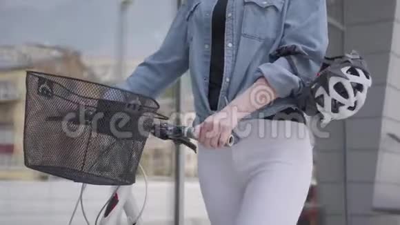 不为人知的年轻运动苗条迷人的金发女郎穿着白色牛仔裤带着自行车靠近商店橱窗视频的预览图