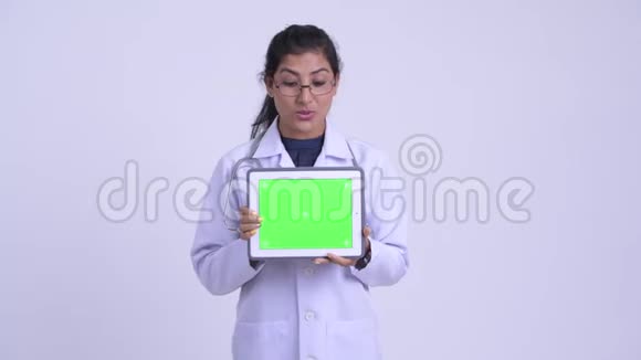 年轻快乐的波斯女医生一边讲一边显示数字平板视频的预览图