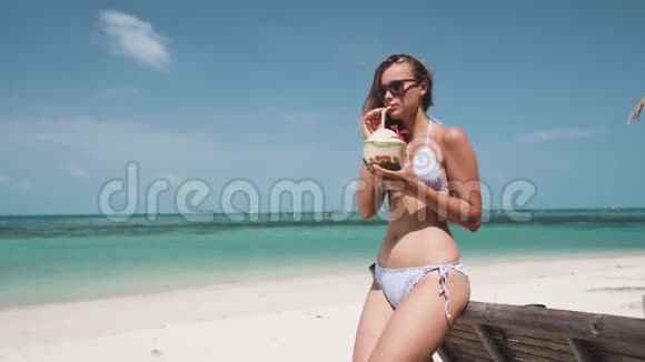 在海滩上戴着墨镜喝椰子酒的女人视频的预览图