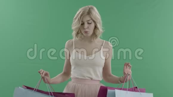 美丽的金发女郎双手拿着购物袋对着绿色的屏幕视频的预览图