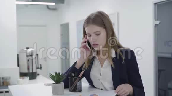 在办公室里站在柜台前一位穿着正式服装的关心的年轻女士通过手机检查文件交谈妇女视频的预览图