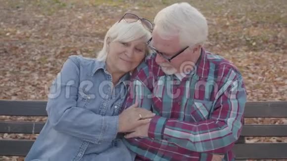 一对高加索老夫妇坐在长凳上说话的肖像成熟的丈夫安抚他美丽的年长者视频的预览图