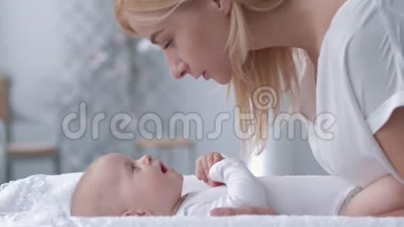 可爱的时刻妈妈亲吻并与一个躺在换桌子上的新生女婴在一起玩得很开心视频的预览图
