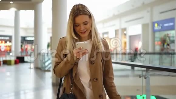 年轻女孩在她的手机里输入一些东西带着购物袋在商场里走来走去视频的预览图